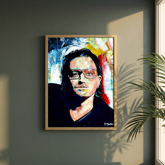 Vibrant Bono U2 framed print in a natural oak frame on a dark green wall beside a window, dappled plant shadow