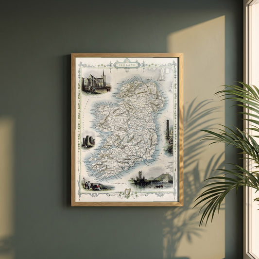 Old Map of Ireland framed print in a natural oak frame on a dark green wall beside a window, dappled plant shadow
