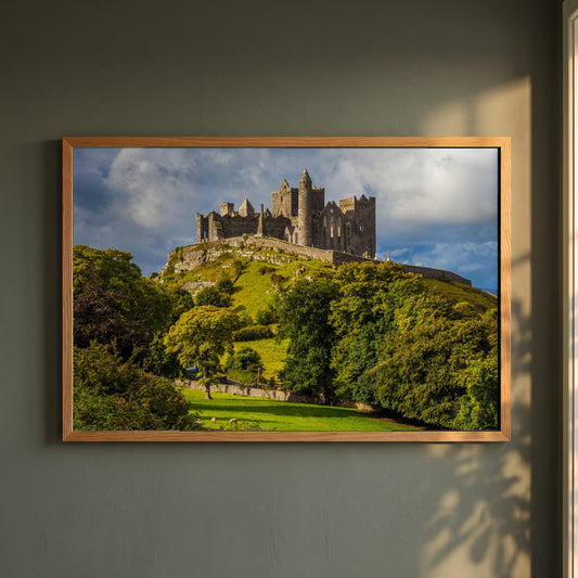 Rock of Cashel framed print in a natural oak frame on a dark green wall beside a window, dappled plant shadow