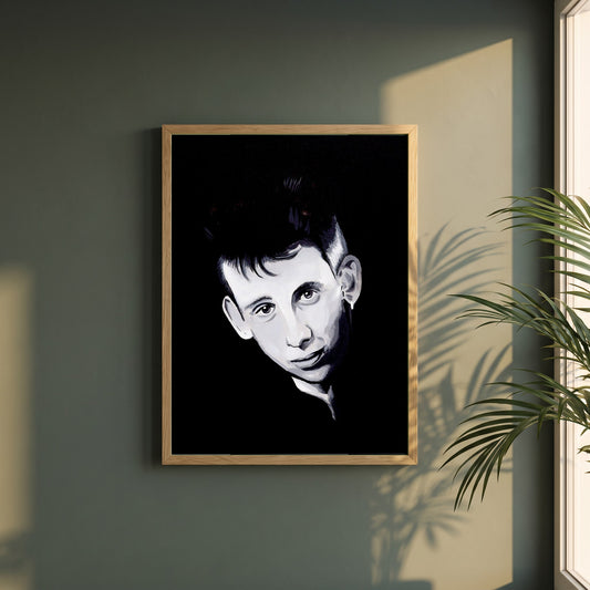 Shane MacGowan framed print in a natural oak frame on a dark green wall beside a window, dappled plant shadow