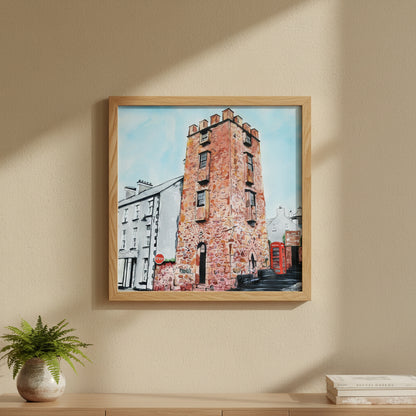 30×30 cm natural oak-framed art print of The Curfew Tower Cushendall hanging in a warm Scandinavian-Irish interior, textured wall, earthy tones, greenery accents, premium lifestyle décor photo with focus on wood grain and matte print texture.