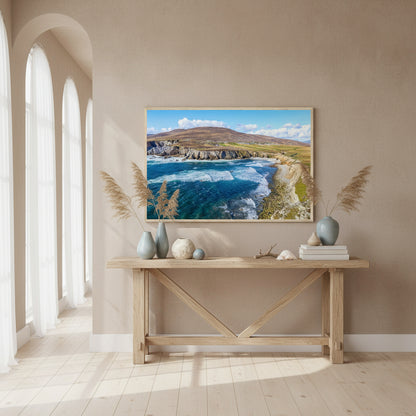 Achill Island print displayed above a console table with sea grasses, ceramic vases and stone textures; muted coastal tones and natural light from tall windows.
