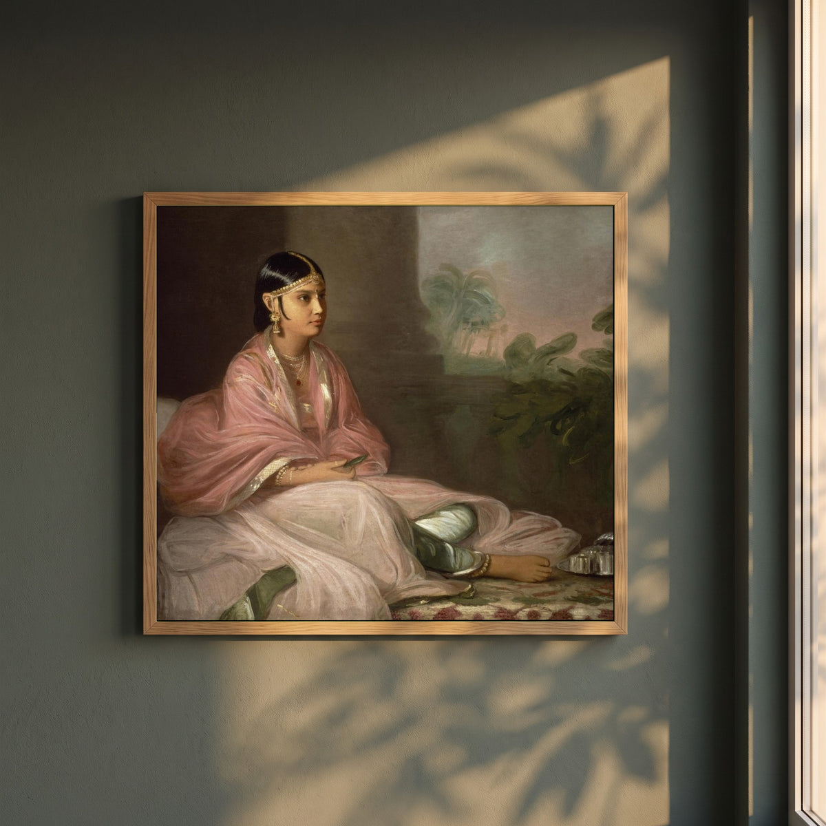 An Indian Lady framed print in a natural oak frame on a dark green wall beside a window, dappled plant shadow
