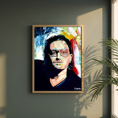 Vibrant Bono U2 framed print in a natural oak frame on a dark green wall beside a window, dappled plant shadow