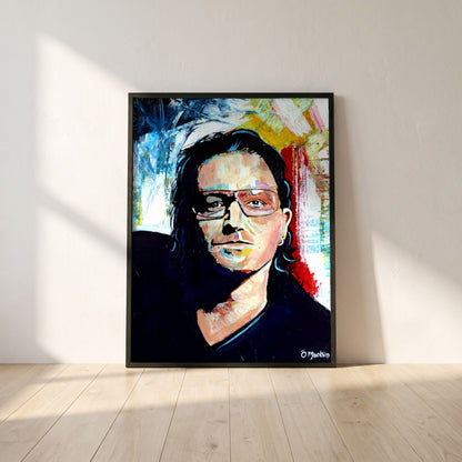 Vibrant Bono U2 framed print in a black frame leaning against a white plaster wall on oak floorboards in morning light