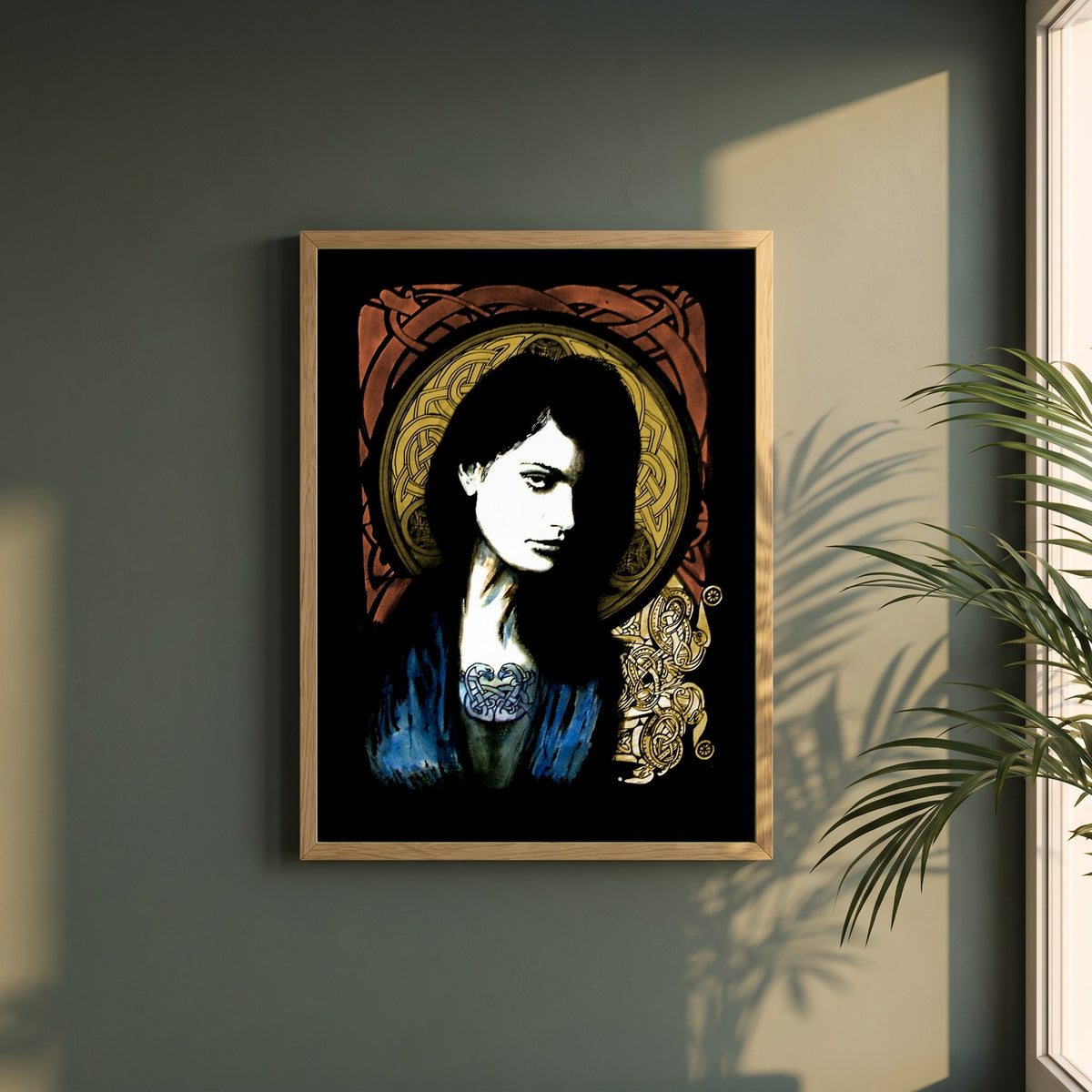 Celtic Goddess framed print in a natural oak frame on a dark green wall beside a window, dappled plant shadow