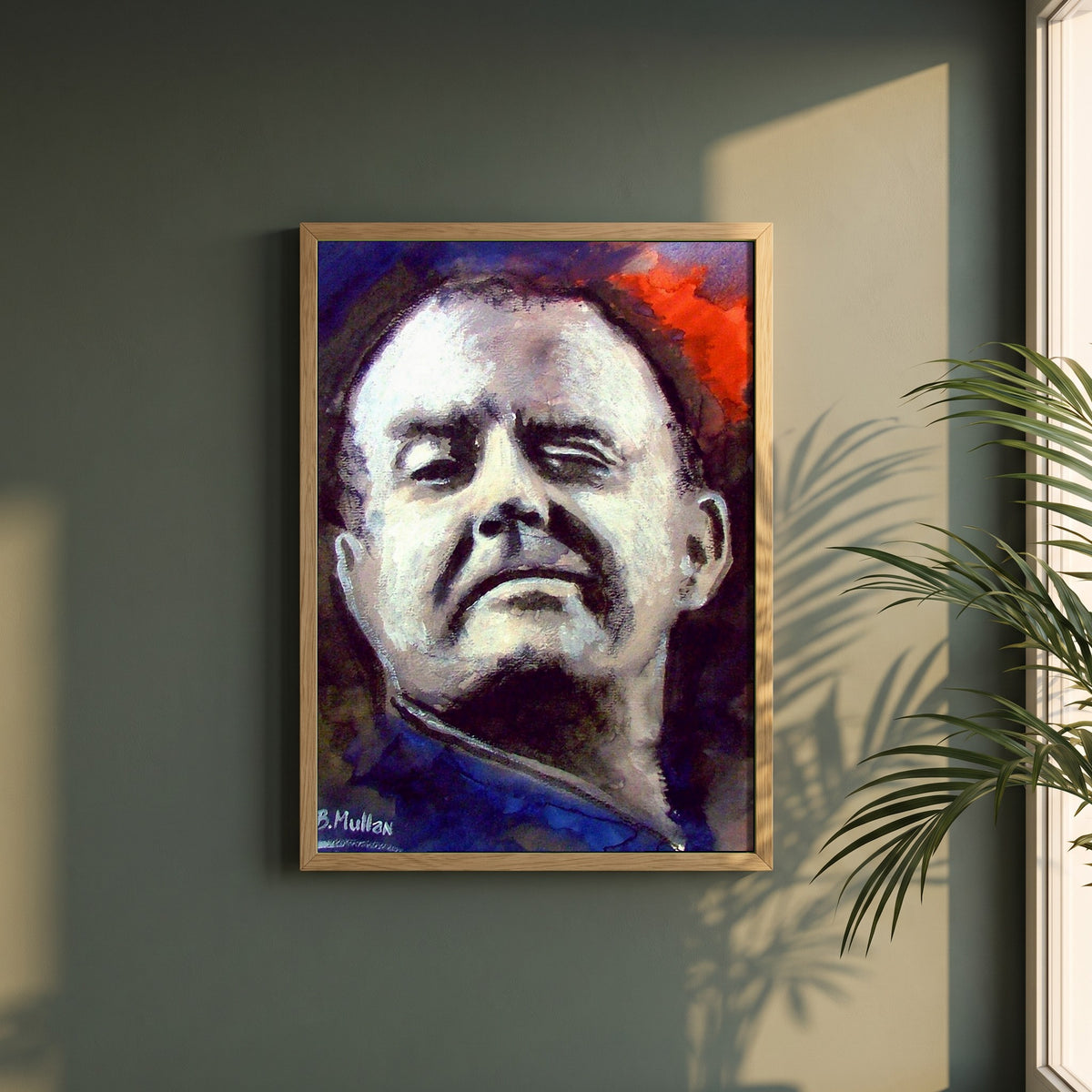 Christy Moore framed print in a natural oak frame on a dark green wall beside a window, dappled plant shadow
