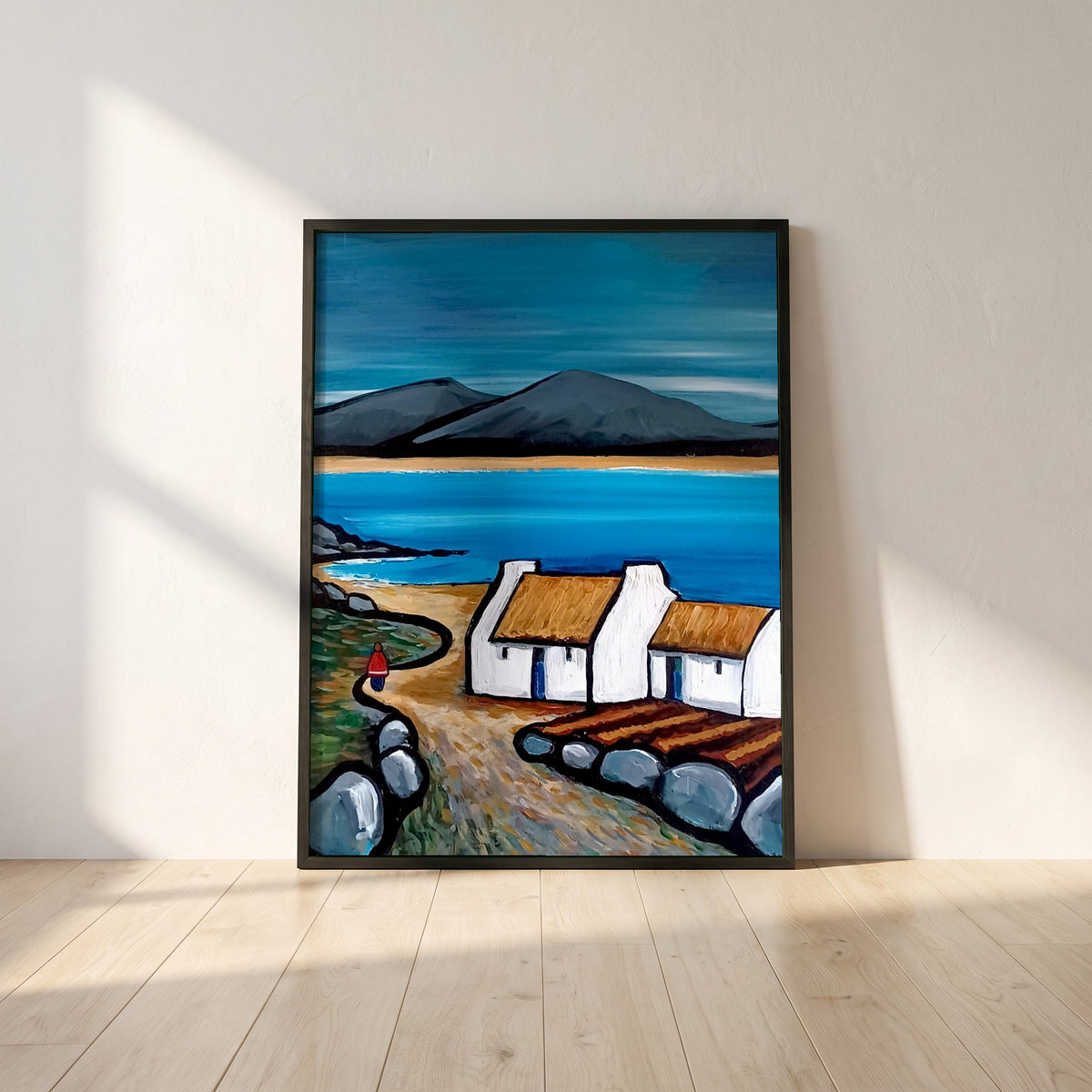 Connemara Lakes Cottage framed print in a black frame leaning against a white plaster wall on oak floorboards in morning light