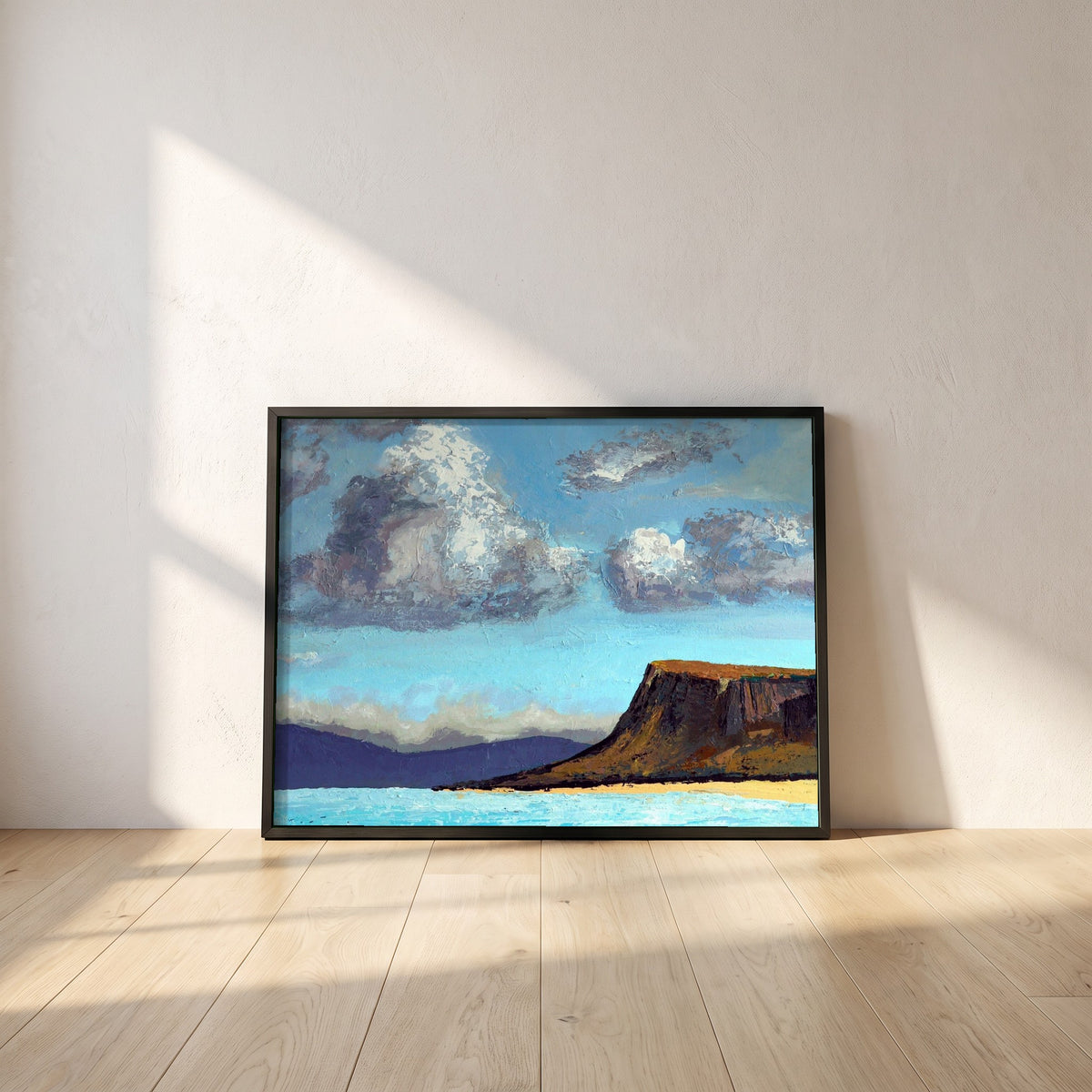 Fair Head from the Sea framed print in a black frame leaning against a white plaster wall on oak floorboards in morning light