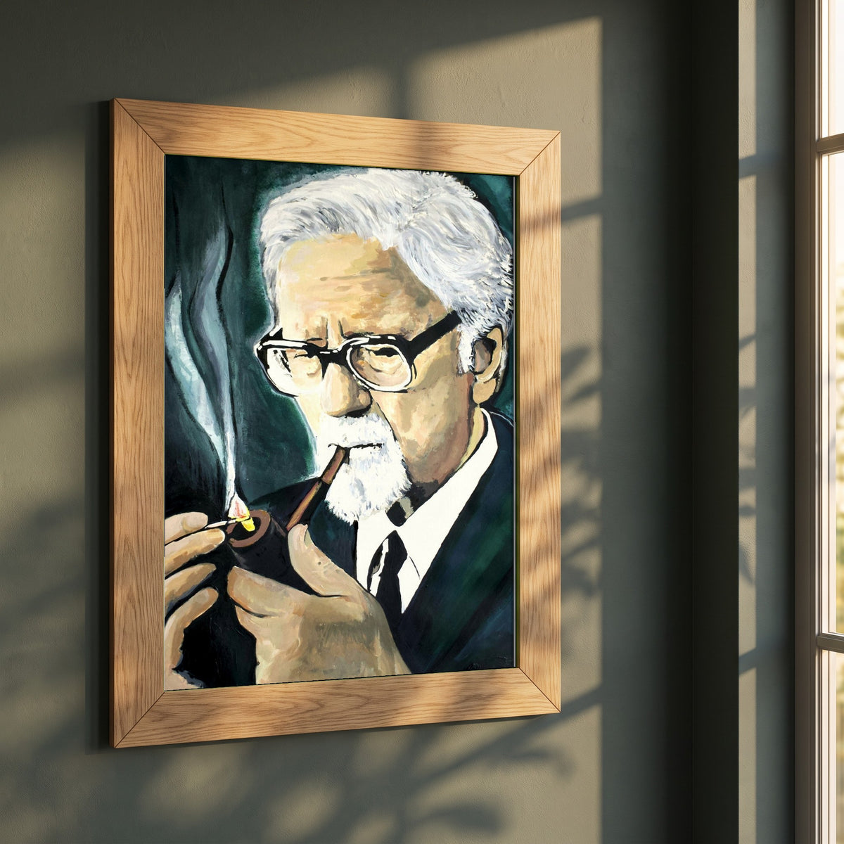 John Hewitt framed print in a natural oak frame on a dark green wall beside a window, dappled plant shadow