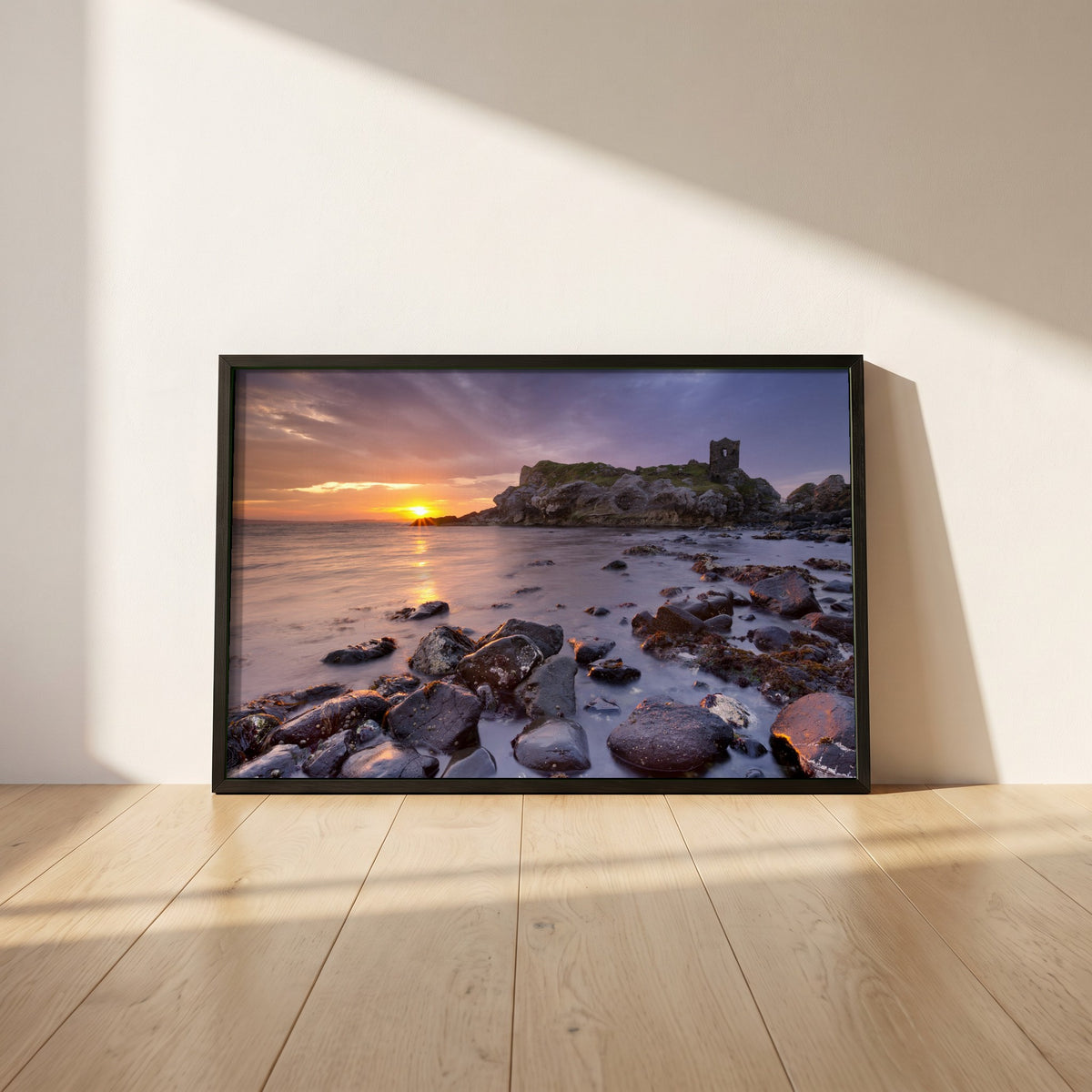 Kinbane Castle Ireland Photography framed print in a black frame leaning against a white plaster wall on oak floorboards in morning light