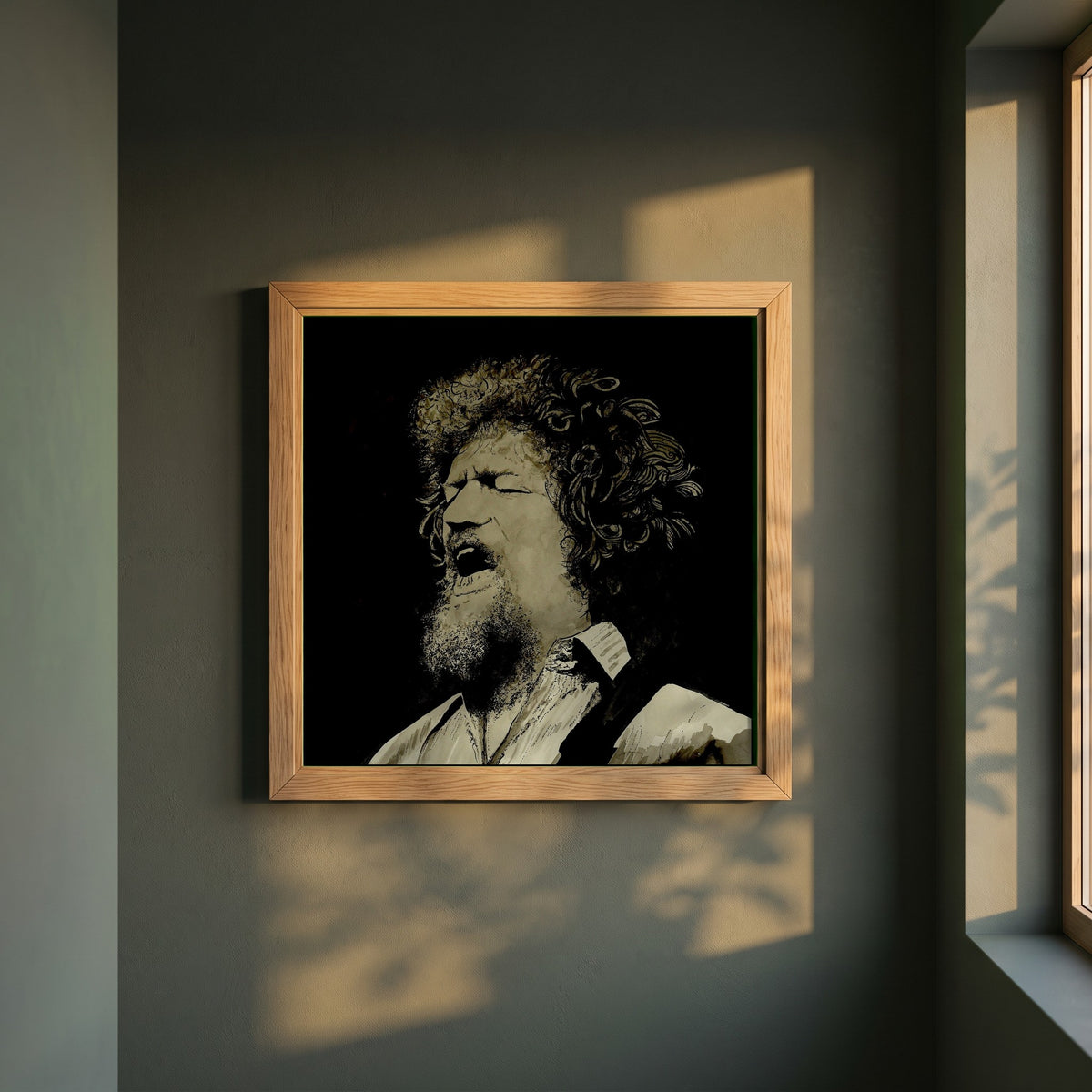 Luke Kelly framed print in a natural oak frame on a dark green wall beside a window, dappled plant shadow