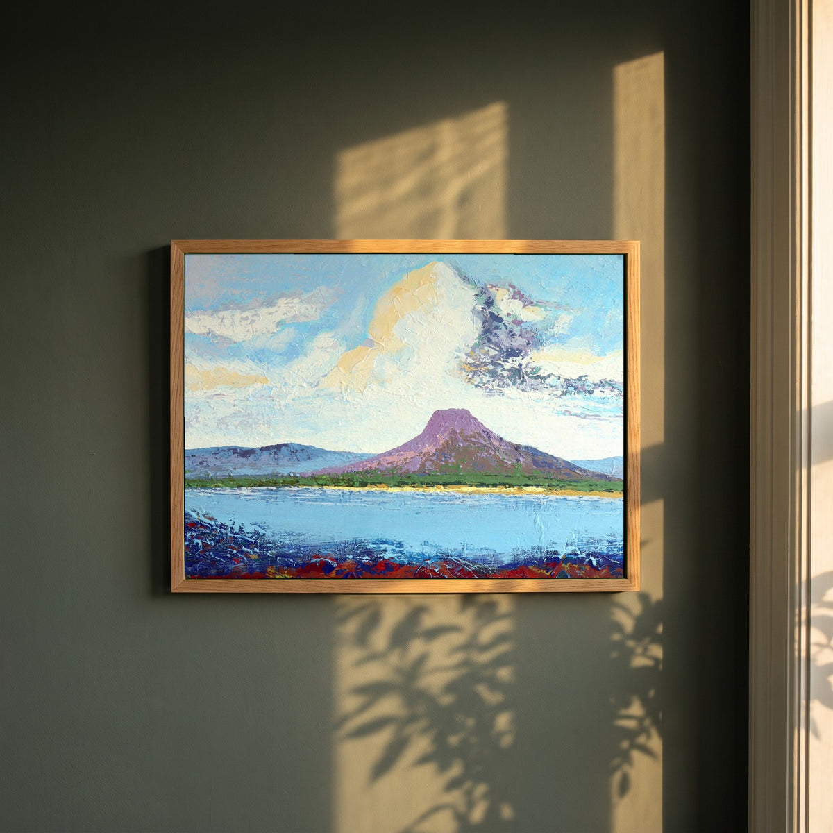 Lurig from the Shore framed print in a natural oak frame on a dark green wall beside a window, dappled plant shadow