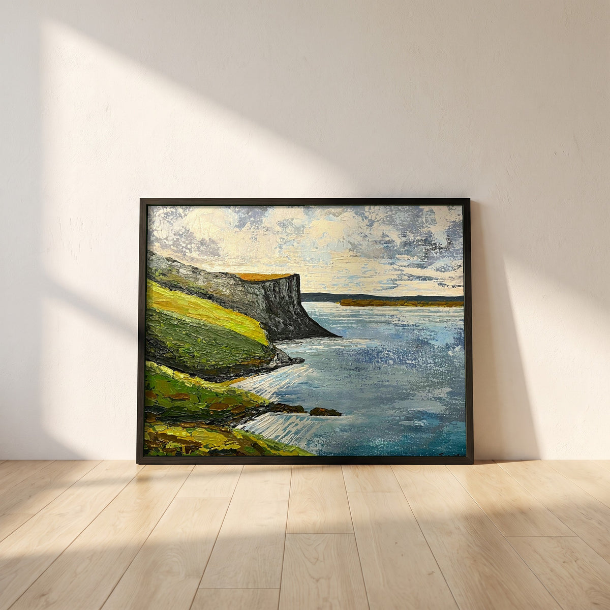 Murlough Bay & Fair Head framed print in a black frame leaning against a white plaster wall on oak floorboards in morning light