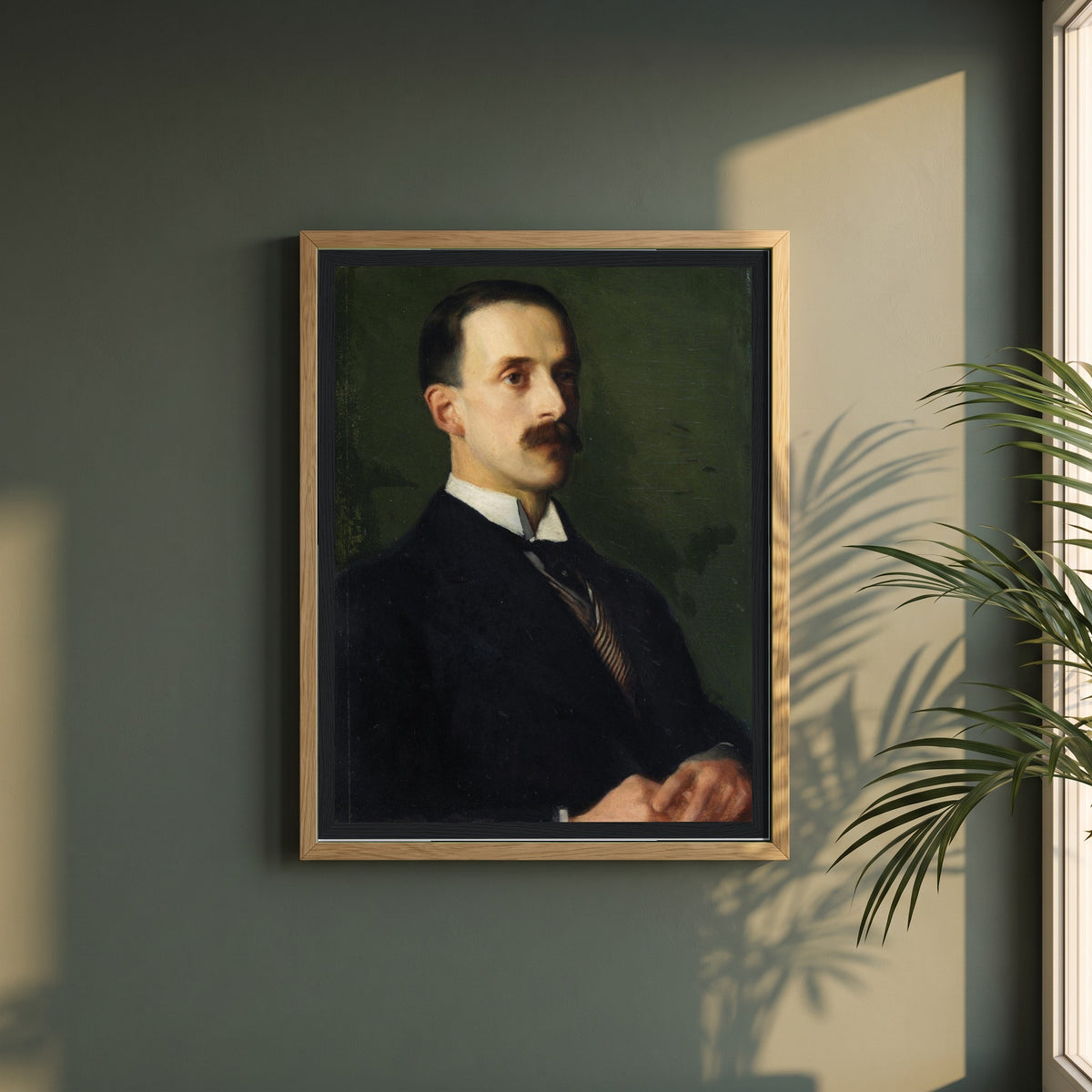 Portrait of Sir Hugh Lane framed print in a natural oak frame on a dark green wall beside a window, dappled plant shadow