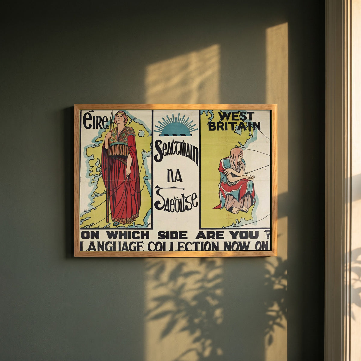 Seachtain na Gaeilge framed print in a natural oak frame on a dark green wall beside a window, dappled plant shadow