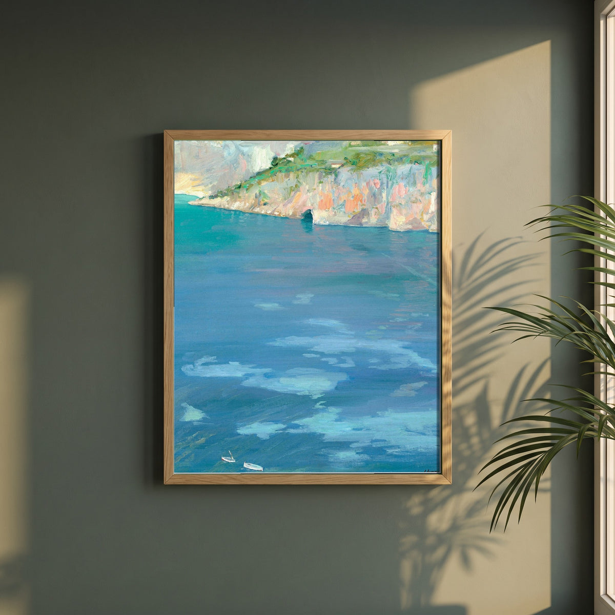 The Little White Boats, Cap Ferrat framed print in a natural oak frame on a dark green wall beside a window, dappled plant shadow