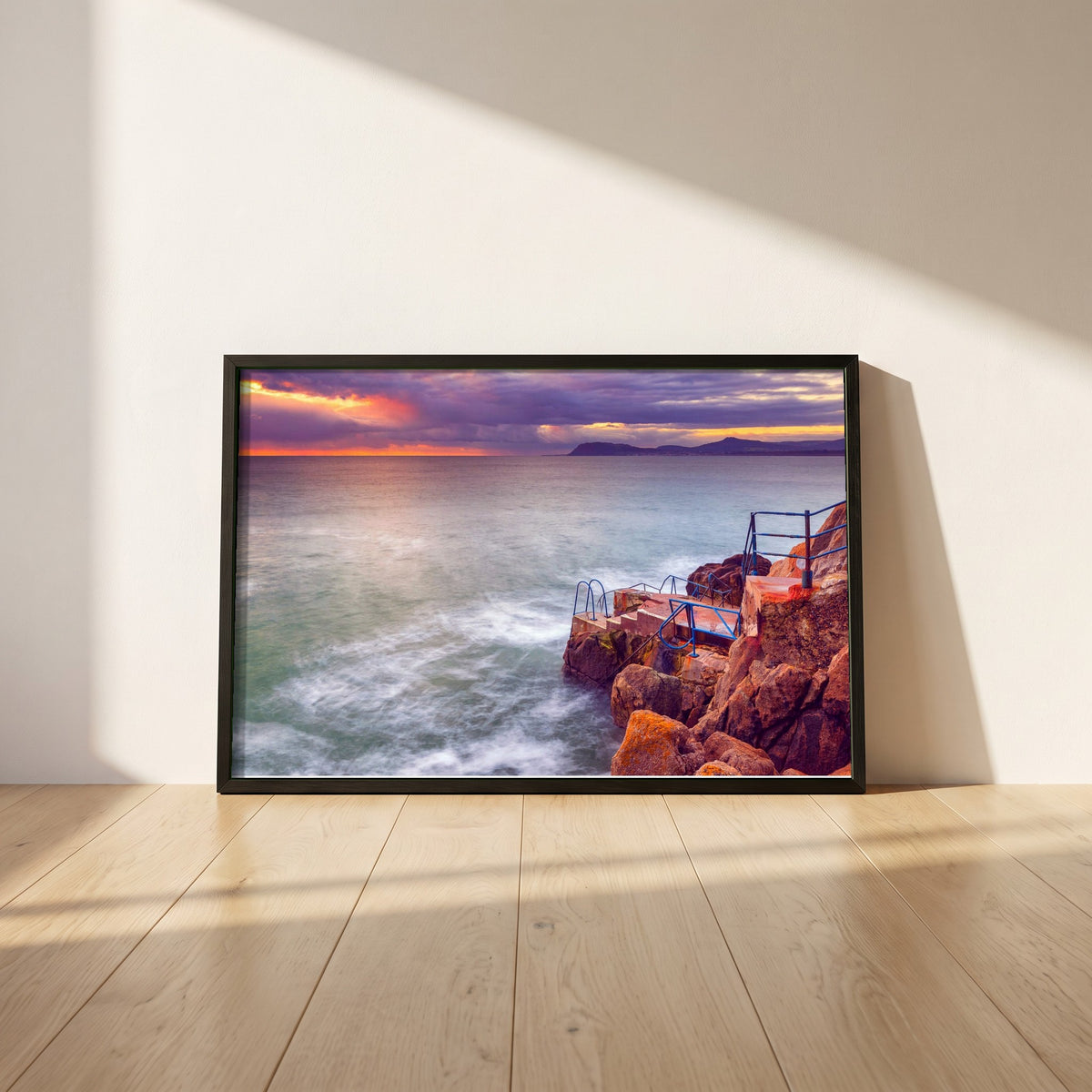 Vico Swimming Dalkey framed print in a black frame leaning against a white plaster wall on oak floorboards in morning light